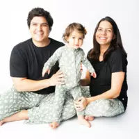 A mom & dad wearing Adult Bamboo Lounge Pants, Stay Sharp sit with a baby in a matching onesie on a white background.