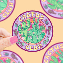 Load image into Gallery viewer, A hand with pink nails holds a Cactus Club vinyl sticker by Turtle Soup, featuring green cacti on a vibrant purple background.
