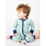 A young child in an Emerson and Friends Sleeper, Baseball Buddies onesie with a two-way zipper sits on the floor near sunglasses.