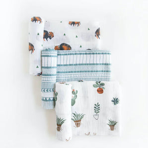 Set of three folded muslin swaddles by Little Unicorn with bison, geometric lines, and potted plants on white.