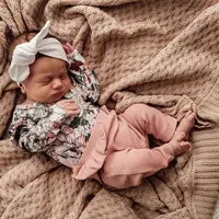 Load image into Gallery viewer, A baby sleeps on a beige blanket in a floral top, Snuggle Hunnys Rose organic pants, and a white bow headband.
