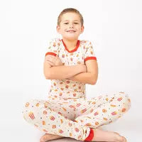 Load image into Gallery viewer, Child smiling cross-legged in buttery soft Emerson and Friends Here For the Snacks bamboo PJs, popcorn pattern, white with red trim.
