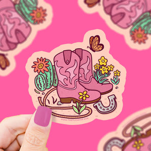 Illustration of pink cowboy boots with flowers, cactus, and butterfly. A hand with pink nails holds Turtle Soups durable vinyl sticker.