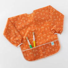 Load image into Gallery viewer, Bumkins Long-Sleeved Art Smock: Grounded holds two paintbrushes in the front pocket, laying flat on a white background.
