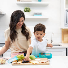 Load image into Gallery viewer, A woman and child in a kitchen making lunch, with the child reaching for fruit near a Bumkins Silicone Bento Box 3 Section: Blue Jelly.
