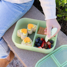 Load image into Gallery viewer, A child eats fruit and sandwiches from a Bumkins Silicone Bento Box 3 Section: Green Jelly with a fork outdoors.
