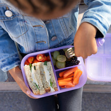 Load image into Gallery viewer, A child wearing a denim jacket with a Bumkins Silicone Bento Box 3 Section: Purple Jelly, filled with a sandwich, fruits, and veggies.
