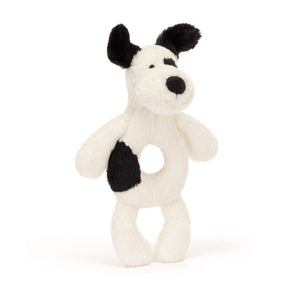 Jellycat Ring Rattle Black & Cream Puppy: a soft-textured plush rattle with a cream body, black ears, and a black patch on its side.