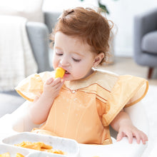 Load image into Gallery viewer, A toddler sits in a high chair, wearing a Bumkins Ruffle Apron Bib: Belle and eating from a gray plate in a bright room.

