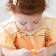 Load image into Gallery viewer, Close-up of a toddler with red hair in a Bumkins Ruffle Apron Bib: Belle looking down, holding an orange fruit.
