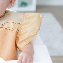Load image into Gallery viewer, Close-up of a child in a high chair wearing a Bumkins Ruffle Apron Bib: Belle, with focus on the ruffle sleeve.
