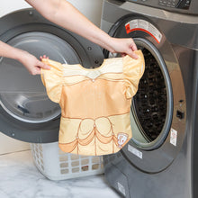 Load image into Gallery viewer, A person holds a Bumkins Ruffle Apron Bib: Belle in front of an open front-loading washing machine.
