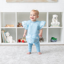 Load image into Gallery viewer, A baby smiles, wearing a Bumkins Ruffle Apron Bib: Cinderella while standing in front of shelves with toys and books.
