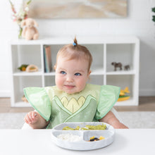 Load image into Gallery viewer, A baby in a Bumkins Ruffle Apron Bib: Tiana sits at a white table with a gray plate of food, looking off to the side with a soft smile.
