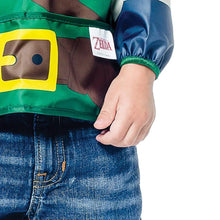Load image into Gallery viewer, Close-up of a child wearing a Bumkins Sleeved Bib: Zelda™ on a white background, with focus on the front pocket and elastic sleeve cuff.

