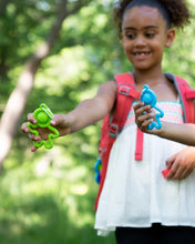 Load image into Gallery viewer, A child outdoors, wearing a red backpack, holds up green &amp; blue toy figures with arms extended and a Fat Brain Toy Co Lil Dimpl Keychain.
