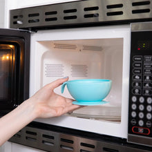 Load image into Gallery viewer, A person places a Bumkins Silicone First Feeding Set: Blue into an open microwave.
