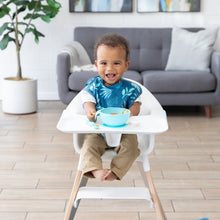 Load image into Gallery viewer, A boy beams in a high chair, wearing a Bumkins SuperBib® 3 Pack: Hangry, Dinosaurs, Blue Tropic with a blue bowl on the tray.
