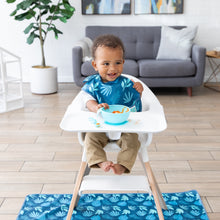 Load image into Gallery viewer, A baby eats from a Bumkins Silicone First Feeding Set: Blue, wearing a dark blue bib in a high chair with a matching mat on the floor.
