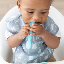 Load image into Gallery viewer, A young boy with a messy face wearing a gray bib chews a Bumkins Silicone Dipping Spoons 3 Pack: Gumdrop while in a high chair.
