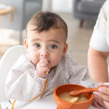 Load image into Gallery viewer, A baby sucks their thumb as an adult hand feeds them from a Bumkins Silicone First Feeding Set: Clay.
