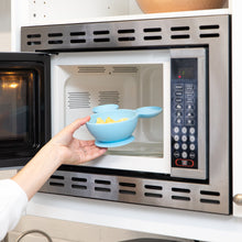 Load image into Gallery viewer, A hand places a Bumkins Silicone First Feeding Set: Mickey Mouse Light Blue filled with food into an open microwave.
