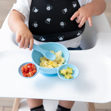 Load image into Gallery viewer, A toddler in a high chair eats scrambled eggs, tomatoes, and avocado from a Bumkins Silicone First Feeding Set: Mickey Mouse Light Blue.
