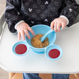 A child enjoys applesauce in a Bumkins Silicone First Feeding Set: Mickey Mouse Light Blue while sitting in a highchair.