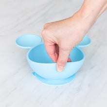 Load image into Gallery viewer, A hand lifts a Bumkins Silicone First Feeding Set: Mickey Mouse Light Blue on a marble surface, showcasing the suction cup bottom.
