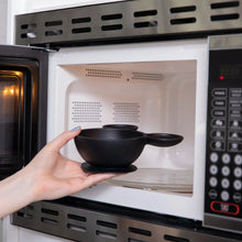 Load image into Gallery viewer, A hand places a Bumkins Silicone First Feeding Set: Mickey Mouse Classic Black into an open microwave.

