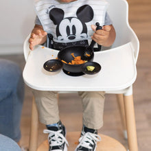 Load image into Gallery viewer, A child in a high chair enjoys mashed sweet potatoes from a Bumkins Silicone First Feeding Set: Mickey Mouse Classic Black.
