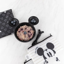 Load image into Gallery viewer, Bumkins Silicone First Feeding Set: Mickey Mouse Classic Black with berries and oatmeal sits near black &amp; white pouches on a marble surface.
