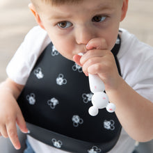 Load image into Gallery viewer, A toddler with brown hair wears a black bib while chewing a spoon from Bumkins Silicone First Feeding Set: Mickey Mouse Vanilla Sprinkle.
