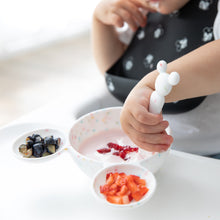 Load image into Gallery viewer, A child in a high chair enjoys yogurt with berries using a Bumkins Silicone First Feeding Set: Mickey Mouse Vanilla Sprinkle.
