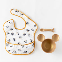Load image into Gallery viewer, Bumkins Silicone First Feeding Set: Minnie Mouse Gold rests next to a black &amp; white Minnie Mouse-themed bib on a white background.
