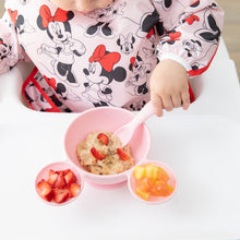 Load image into Gallery viewer, A child enjoys oatmeal with strawberries from a Bumkins Silicone First Feeding Set: Minnie Mouse Light Pink while seated in a high chair.
