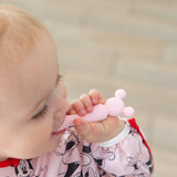 A baby in a bib chews on a spoon from Bumkins Silicone First Feeding Set: Minnie Mouse Light Pink.