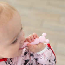 Load image into Gallery viewer, A baby in a bib chews on a spoon from Bumkins Silicone First Feeding Set: Minnie Mouse Light Pink.

