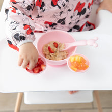 Load image into Gallery viewer, A child enjoys oatmeal with fruit from Bumkins Silicone First Feeding Set: Minnie Mouse Light Pink on their high chair tray.
