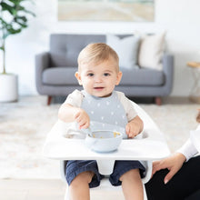 Load image into Gallery viewer, A toddler in a high chair wears a gray silicone bib and eats from a Bumkins Silicone First Feeding Set: Gray with an adult nearby.
