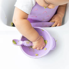 Load image into Gallery viewer, A baby in a high chair eats mashed avocado from a Bumkins Silicone First Feeding Set: Lavender while wearing a matching silicone bib.
