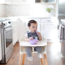 Load image into Gallery viewer, A baby in a high chair uses a Bumkins Silicone Dipping Spoons 3 Pack: Lollipop to eat from a lavender bowl in a bright, modern, kitchen.
