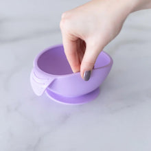 Load image into Gallery viewer, A hand holds a Bumkins Silicone First Feeding Set: Lavender, demonstrating the suction cup bottom on a marble surface.
