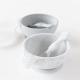 Bumkins Silicone First Feeding Set: Marble sits in front of a gray bowl and spoon set on a white background.