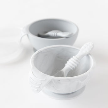 Bumkins Silicone First Feeding Set: Marble sits in front of a gray bowl and spoon set on a white background.