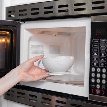 A person places a Bumkins Silicone First Feeding Set: Marble into an open microwave.