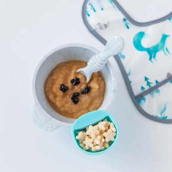 Bumkins Silicone First Feeding Set: Marble with applesauce and berries, a blue cup of star-shaped puffs, and a bib on a white background.