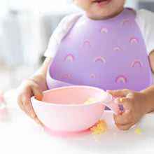 Load image into Gallery viewer, Close-up of a child in a purple silicone bib holding a bowl with eggs from Bumkins Silicone First Feeding Set: Pink.
