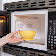 Load image into Gallery viewer, A person places a Bumkins Silicone First Feeding Set: Pineapple into an open microwave.
