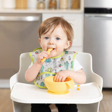 Load image into Gallery viewer, A toddler in a high chair wearing a cactus-print bib eats from a Bumkins Silicone First Feeding Set: Pineapple in a modern kitchen.
